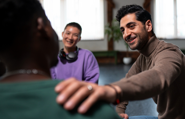 A group of three individuals engage in a serious conversation, with one person offering support by touching another's shoulder